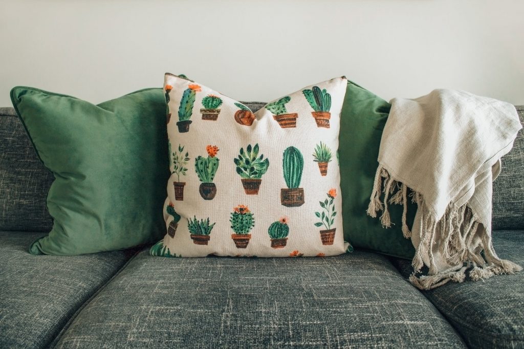 Coussins verts avec des motifs de plantes et couverture en lin posés sur un canapé