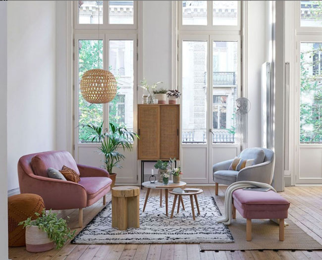 Salon d'appartement avec murs blancs et mobilier bordeau et bleu, luminaire en osier et touches de verdure