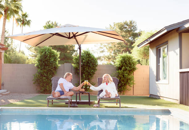 Parasol géant dans un jardin avec piscine, au bord de laquelle un coupe se repose sur des transats